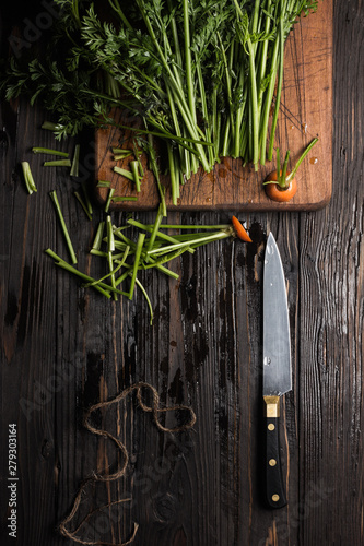 Stalks of carrots, cutting board and knife on rustic table