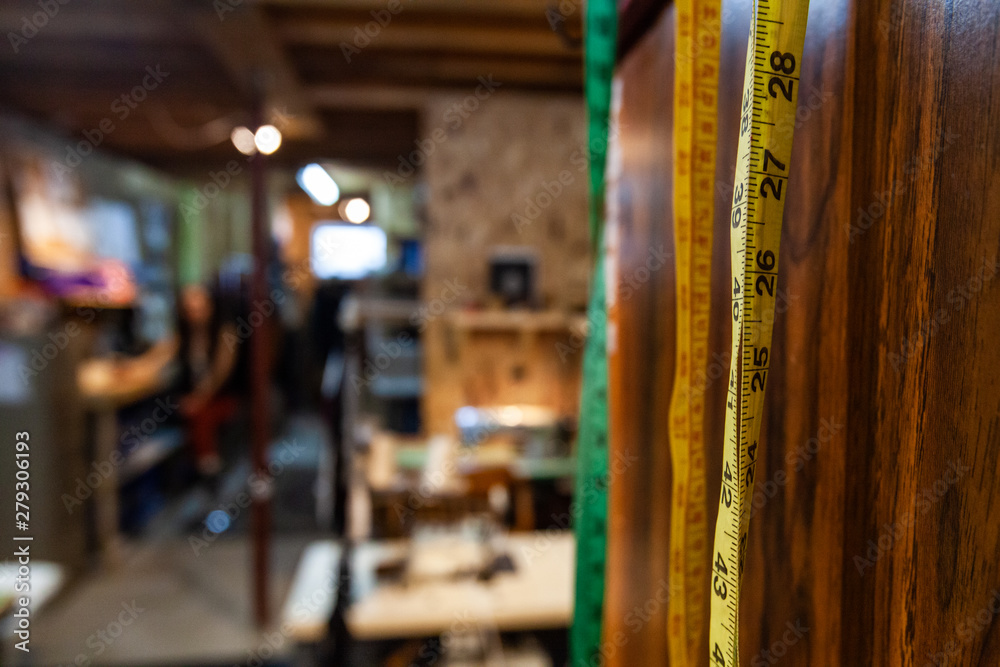 Rulers and sewing machines in a workshop. Measuring tapes are viewed close-up, hung on a wall for easy access in a seamstress studio, blurred background with copy-space to the left.