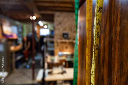 Rulers and sewing machines in a workshop. Measuring tapes are viewed close-up, hung on a wall for easy access in a seamstress studio, blurred background with copy-space to the left. © Valmedia