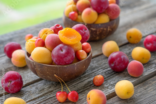 Ripe apricots, plums and cherries in bowl on rustic wooden table	