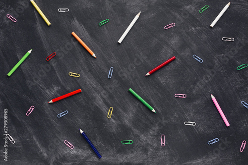 Colourful pencils and paper clips on blackboard