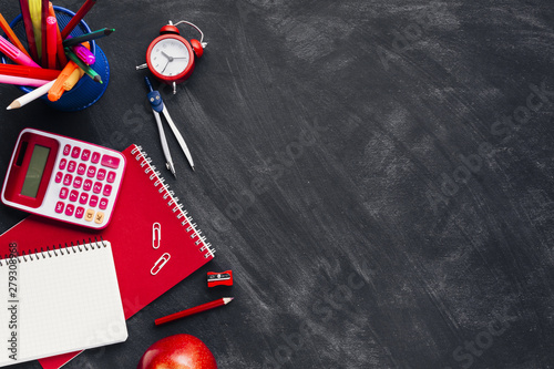 Red stationery near clock and apple on blackboard