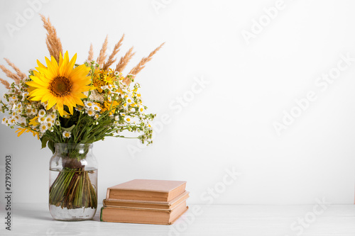 Summer bouquet of wildflowers in glass vase, old books on rustic background. Season design concept. Teachers day concept, back to school.