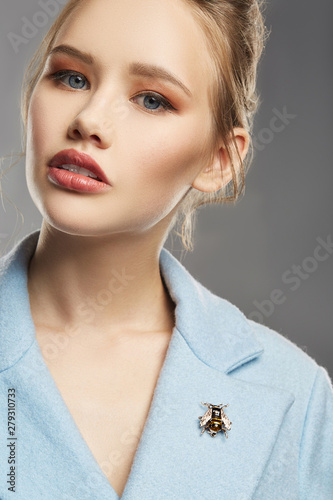 Fotografia Portrait of girl with tied back fair hair, wearing sky blue coat with bright brooch in view of black fly on lapel