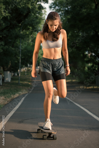 Portrait of a young brunette woman skateboarding on a road in the park. © ianachyrva