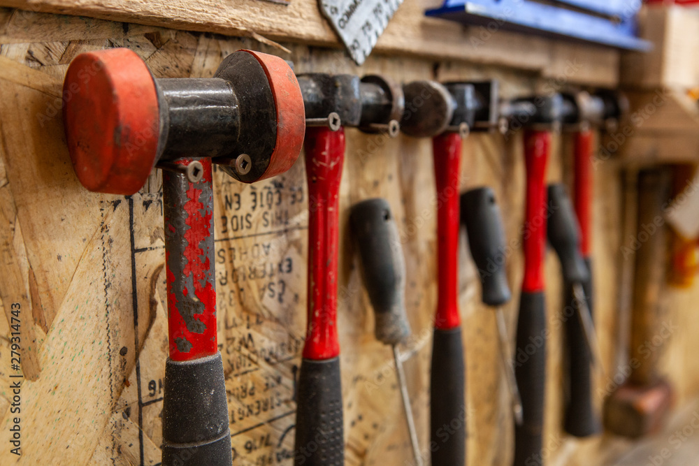 Selection of metalworking mallets. A closeup view on a variety of metalwork hammers and mallets inside a workshop. Various sizes and styles hanging on screws for easy access. Selection of metalworking mallets. A closeup view on a variety of metalwork hammers and mallets inside a workshop. Various sizes and styles hanging on screws for easy access.