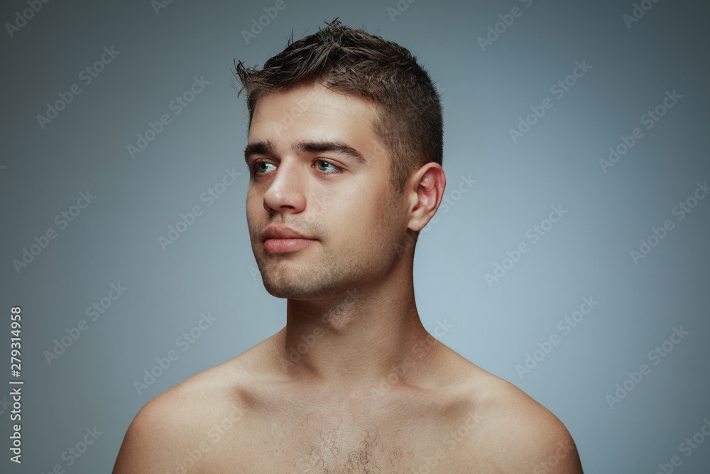 Portrait of shirtless young man isolated on grey studio background. Caucasian healthy male model looking at side and posing. Concept of men's health and beauty, self-care, body and skin care. Portrait of shirtless young man isolated on grey studio background. Caucasian healthy male model looking at side and posing. Concept of men's health and beauty, self-care, body and skin care.
