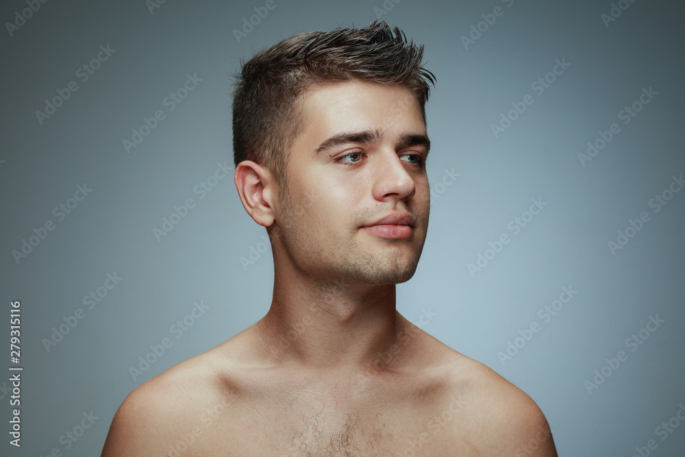 Portrait of shirtless young man isolated on grey studio background. Caucasian healthy male model looking at side and posing. Concept of men's health and beauty, self-care, body and skin care. Portrait of shirtless young man isolated on grey studio background. Caucasian healthy male model looking at side and posing. Concept of men's health and beauty, self-care, body and skin care.