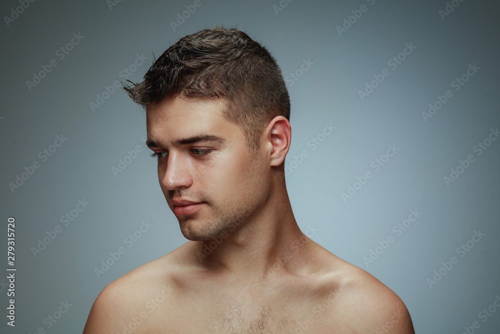 Portrait of shirtless young man isolated on grey studio background. Caucasian healthy male model looking at side and posing. Concept of men's health and beauty, self-care, body and skin care. Portrait of shirtless young man isolated on grey studio background. Caucasian healthy male model looking at side and posing. Concept of men's health and beauty, self-care, body and skin care.