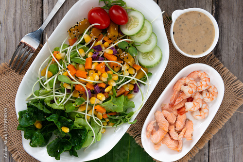 Fresh salad plate with shrimp, salmon, tomato and mixed greens on wooden background .