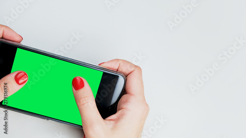 Women's hands holding a cellphone. Green mobile screen, copy space. Smartphone mockup.