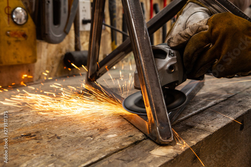 Sparks fly from blacksmith disc grinder. A close up view of an abrasive disc cutter in use. Hands of a skilled worker operate power tool inside a workshop. Hot sparks fly from the abrasive wheel.
