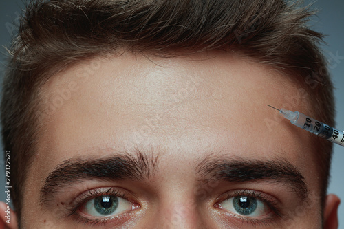 Close-up portrait of young man isolated on grey studio background. Filling botox surgery procedure. Concept of men's health and beauty, cosmetology, self-care, body and skin care. Anti-aging.