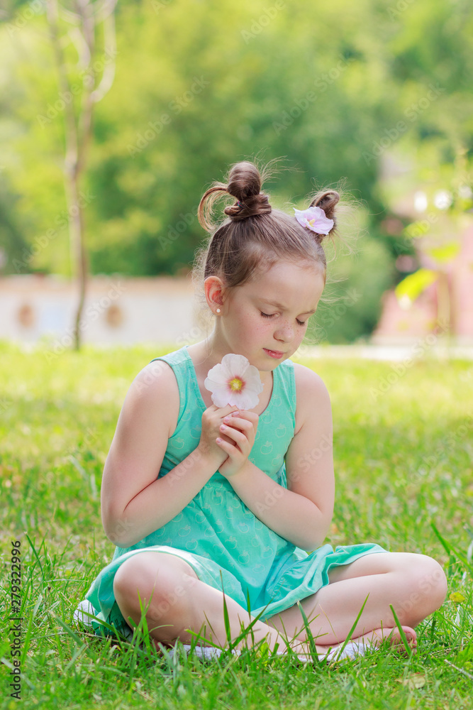 Little beautiful girl sitting on the green grass in the park, soft focus background Little beautiful girl sitting on the green grass in the park, soft focus background