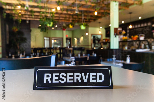 Reserved sign on restaurant table. A table reservation sign is seen close-up inside an eco-friendly establishment. Blurry green foliage and decor is viewed in background with copy space to top.