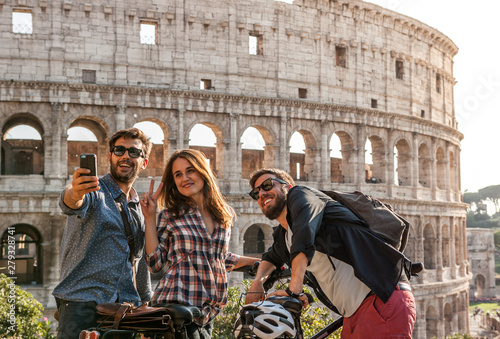 Photography Three happy young friends tourists with bikes at Colosseum in Rome taking pictur