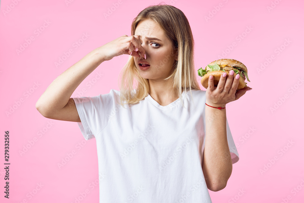 woman with hamburger closed nose on a pink background. fast food woman with hamburger closed nose on a pink background. fast food