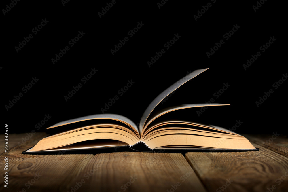 Obraz premium open book on a wooden table and black background with copy space for your text