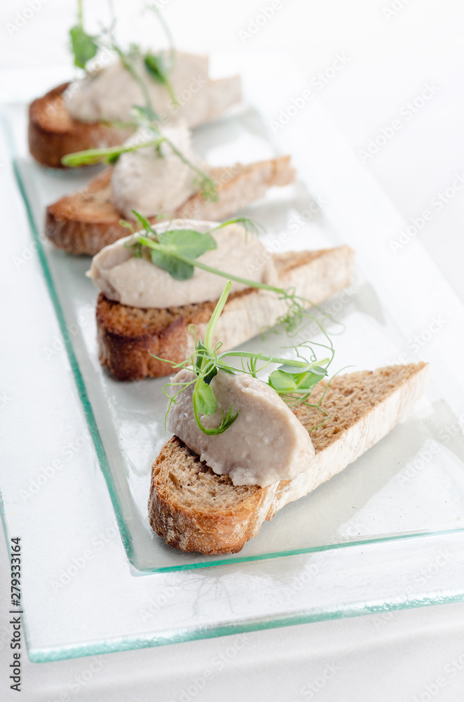 Bruschetta with liver pate and herbs on white table. Canape mini sandwiches Isolated on background. Banquet service with different food snacks and appetizers. Catering food, snacks. Party food.