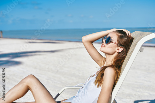 woman in glasses in a white bathing suit lying on an island lounger