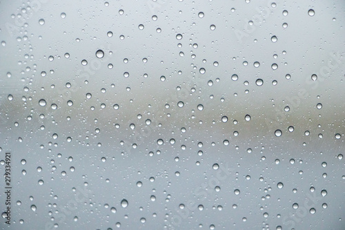 rain drops on window glasses surface through the window with overcast clouds abstract background