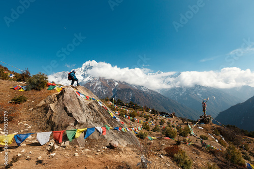 Everest Base Camp Trek. A man stands on a hill and looks at the horizon. In the background are mountains and clouds. In the frame Nepalese prayer flags with prayers.