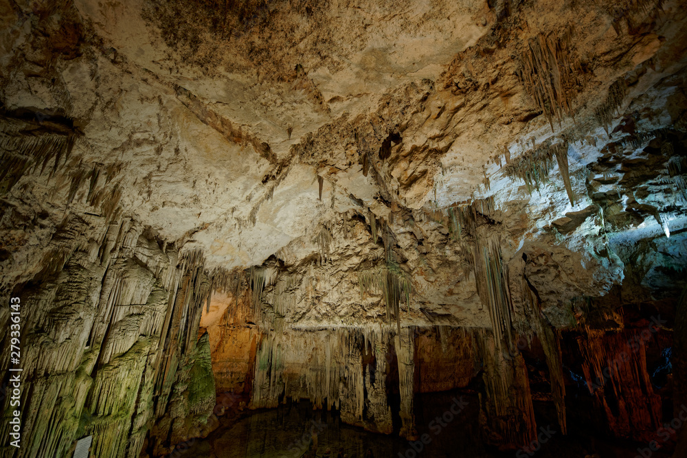 Imposing stalactites and stalacmites reflecting in a small underground lake inside the limestone cave (Tropfsteinhöhle) Grotta di Nettuno in Sardegna (Italy)	