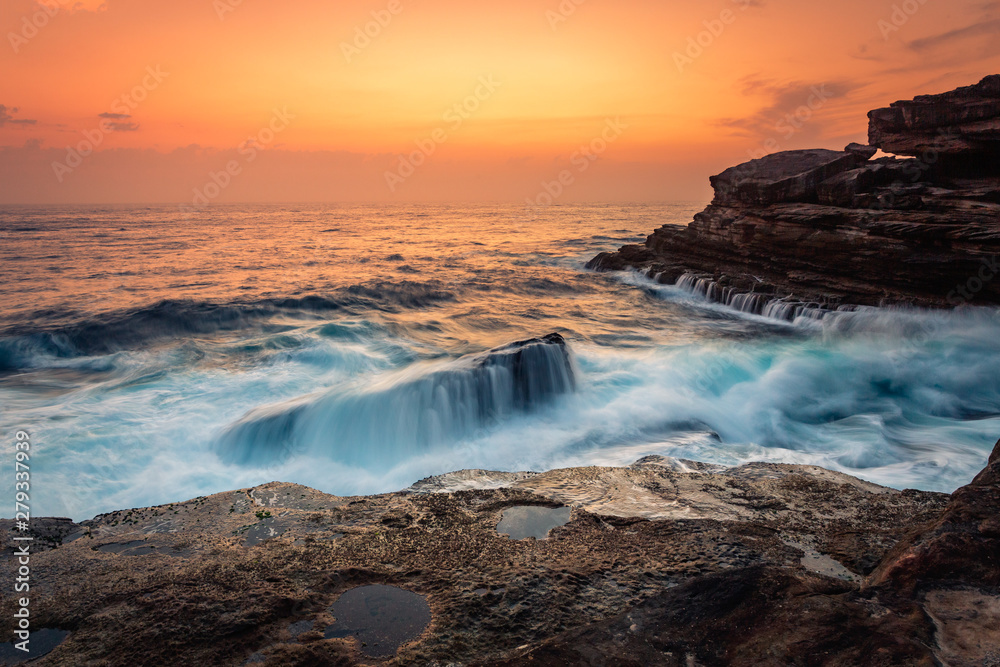 Stunning sunrise and waves crash over rocks on the Sydney sea coast