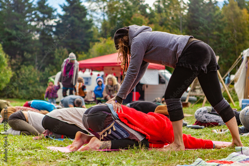 Fusion of cultural & modern music event. People are seen relaxing and stretching in a festival campsite, as a bohemian styled person performs lumbar back massage on one person. - obrazy, fototapety, plakaty 