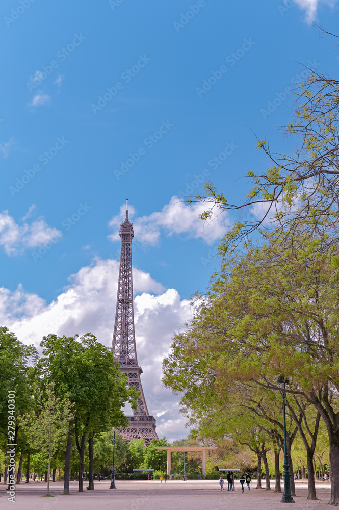 Eiffel tower in the alley and green trees. Spring in Paris. Blue sky and clouds. Travel and tourism.