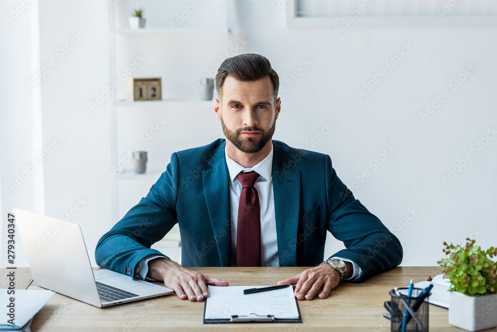 handsome recruiter sitting near clipboard and laptop in office handsome recruiter sitting near clipboard and laptop in office
