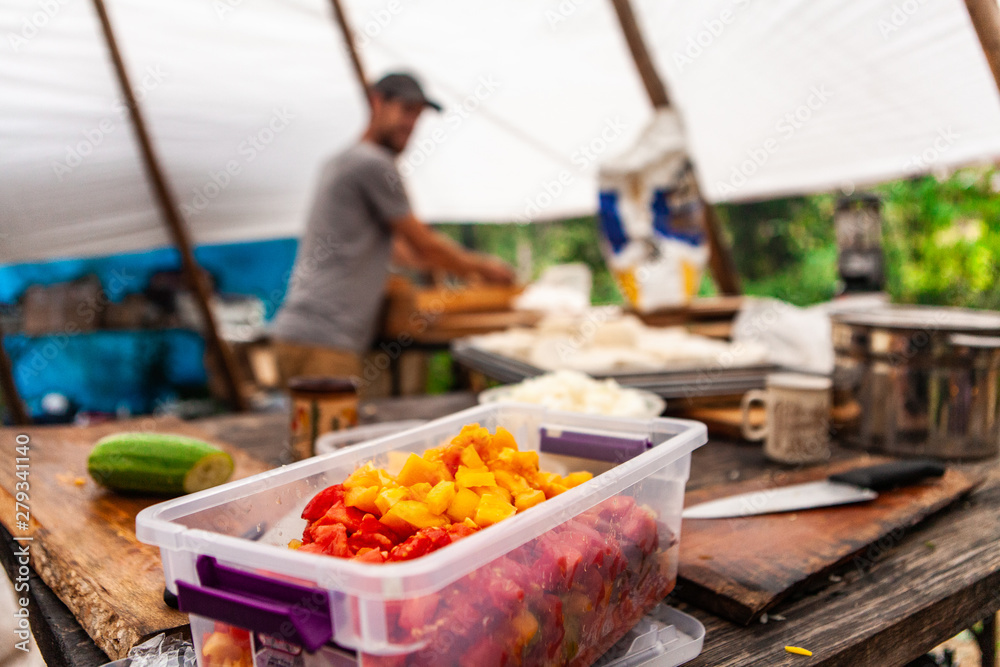 Fusion of cultural & modern music event. A closeup view of chopped vegetables in a plastic container, on a rustic wooden bench inside a tipi tent at a music festival campsite, outdoor food preparation - obrazy, fototapety, plakaty 