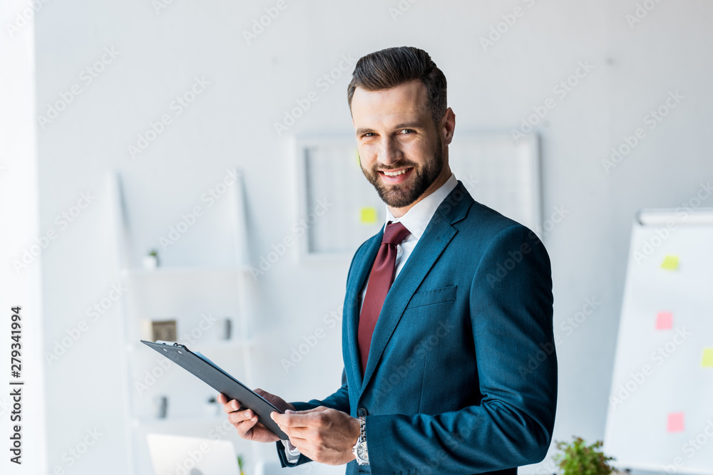 cheerful bearded man in suit holding clipboard in office cheerful bearded man in suit holding clipboard in office