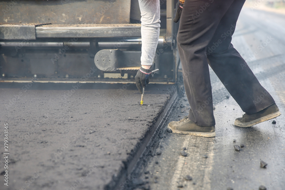 asphalt paving works. road worker checks the depth of paving the roadway asphalt paving works. road worker checks the depth of paving the roadway