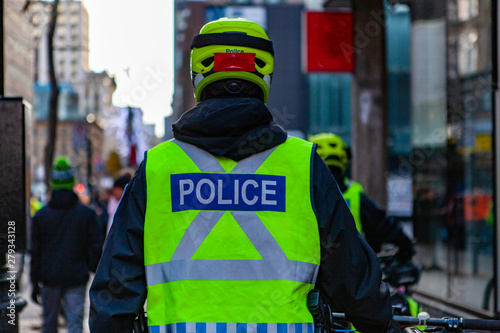 Environmental activists march in city. A police bike patrol is viewed from the back in high visibility uniform and helmet on an urban street, public safety during an ecological protest.