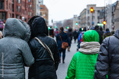 Environmental activists march in city. People wearing hooded winter coats are seen close-up from behind on a busy street during a demonstration, snow flakes are seen falling with a blurry city scene