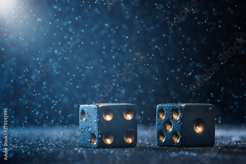 Two black dices illuminated by bright light on a blue background. The concept of gambling.