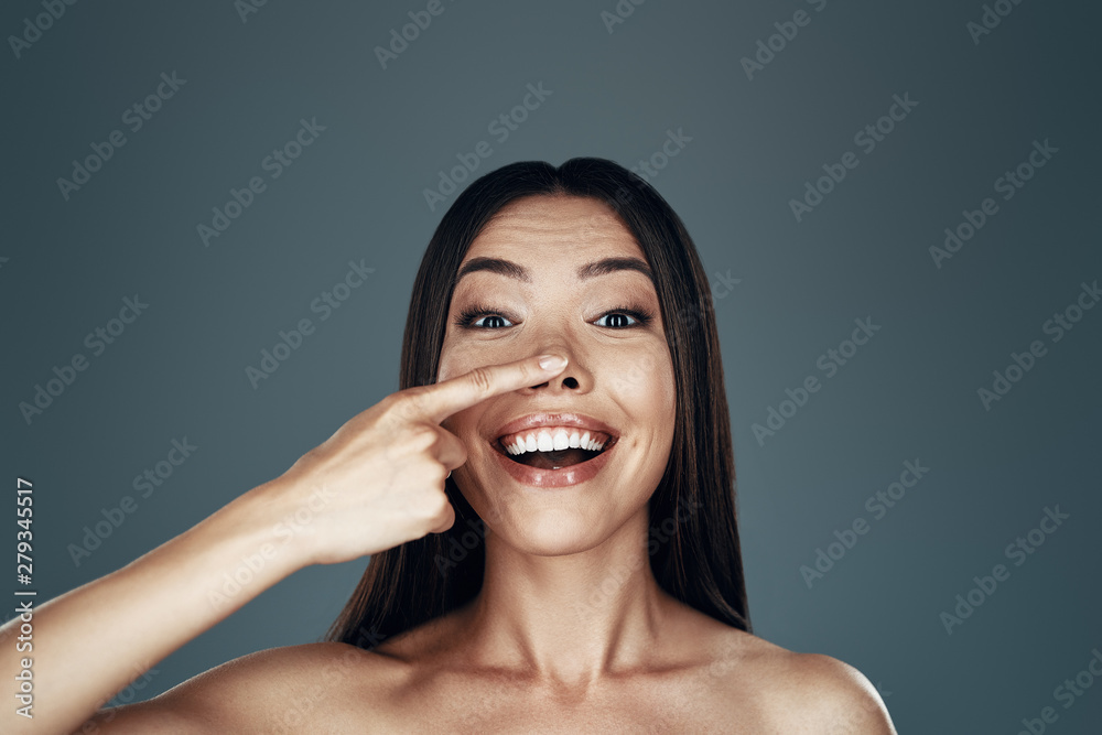 Playful woman. Happy young Asian woman looking at camera and smiling while standing against grey background Playful woman. Happy young Asian woman looking at camera and smiling while standing against grey background