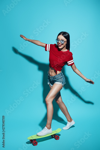 Real fun. Full length of attractive young Asian woman smiling while skateboarding against blue background