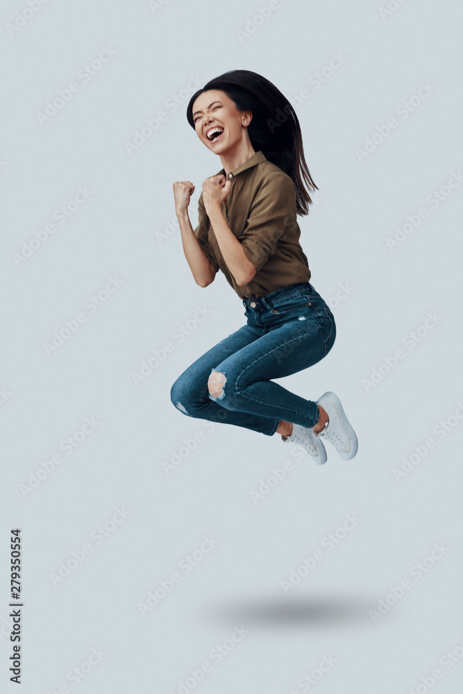 Success. Full length of beautiful young Asian woman gesturing and smiling while hovering against grey background