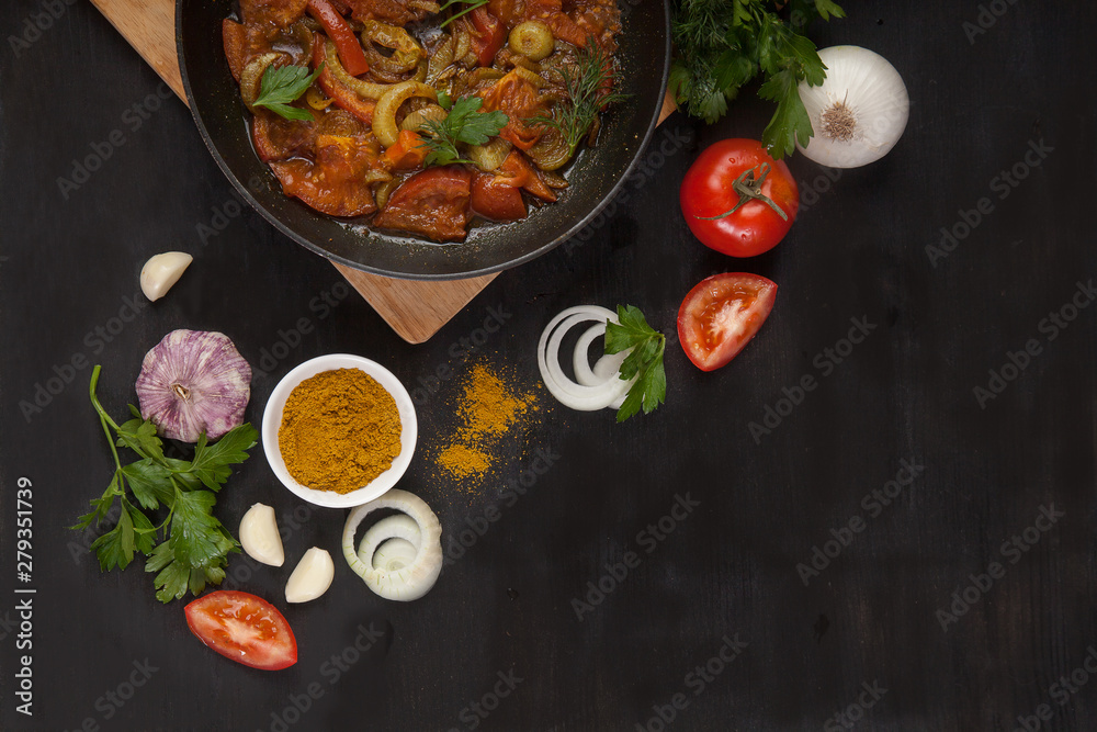 Roasted tomatoes with onions in a pan and fresh vegetables on a black background. Copy spaes.