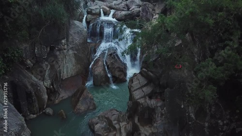 Flying on the drone above the wild waterfall in tropical palm forest. Beautiful landscape of green jungle and stream of mountain river. Cascade of water around nature. Travel concept in Asia.