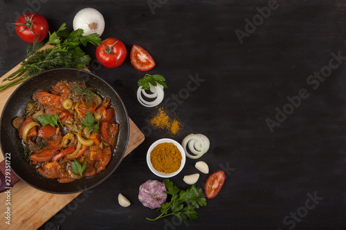 Process of cooking hot tomato sauce for pasta or spaghetti in a pan surrounded by the ingredients: onion, greens, radish, tomato, basil, bell pepper, paprika and red pepper in spoon on wooden table