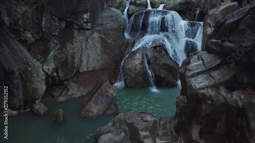 Flying on the drone above the wild waterfall in tropical palm forest. Beautiful landscape of green jungle and stream of mountain river. Cascade of water around nature. Travel concept in Asia.