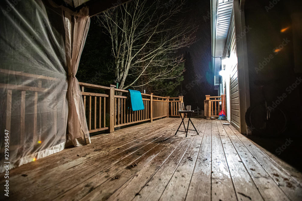 Backyard terrace illuminated by night. A low down perspective of a large  wooden veranda at the back of a residential property, lit-up during late  hours with copy-space in the foreground. Stock Photo
