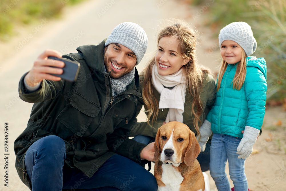 family, pets and people concept - happy mother, father and little daughter with beagle dog taking selfie by smartphone outdoors in autumn