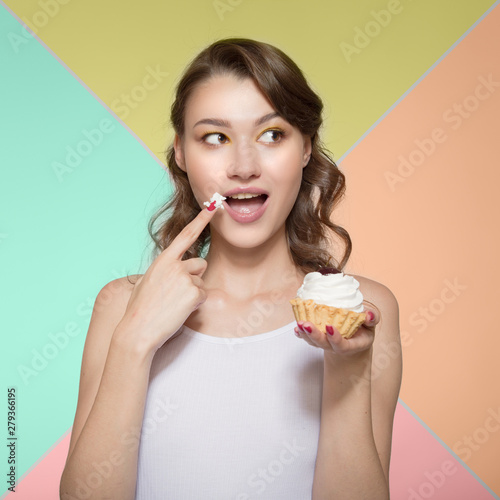 young woman happily eating a sweet dessert. To bring a finger in a sweet cream to a mouth. Colorful bright background