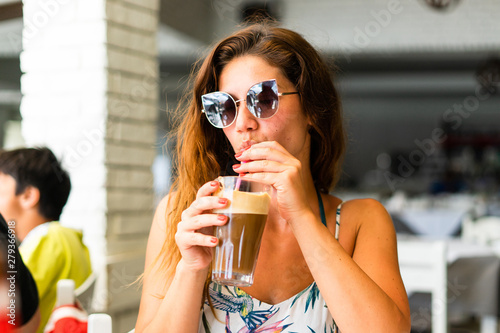 Portrait of young woman at the restaurant drinking frappe coffee in a summer day on the vacation wearing sunglasses photo