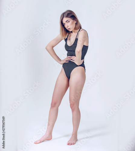Slender girl in boots on a high heel in bodisuit stands in full growth in profile on a light background. Beautiful figure, sexy, confidence.