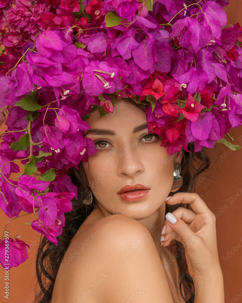 Beauty fashion model girl with pink flower on her head. Portrait on red orange background. Spa and beauty salon concept.